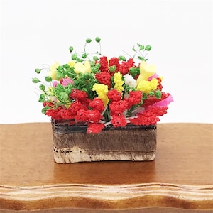 May include: A miniature wooden planter filled with a variety of colorful flowers, including red, yellow, and pink. The planter is sitting on a wooden surface.