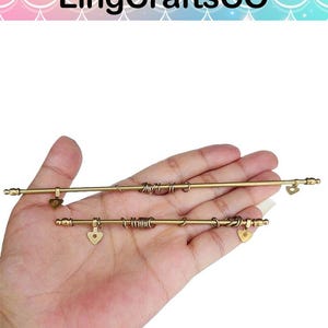 May include: Two gold-coloured metal rods with decorative elements, including heart-shaped charms and coiled wire accents. The rods are held in a hand, showcasing the intricate details and craftsmanship. The top of the image has the text "LingCraftsCO".