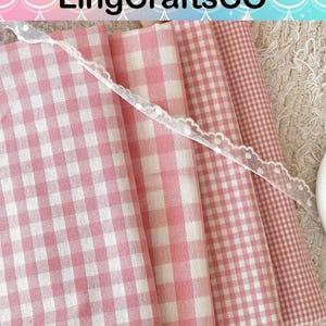 May include: Four folded pieces of fabric featuring various pink and white gingham check patterns, ranging from large to small squares. A thin, white, semi-sheer lace ribbon with a scalloped edge is draped diagonally across the fabric layers.