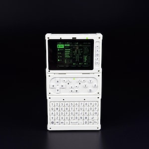 Puede incluir: Un dispositivo electrónico portátil de color blanco con una pantalla rectangular que muestra una interfaz digital verde con un diagrama del cuerpo humano. Debajo de la pantalla hay un panel de control con botones direccionales y un teclado QWERTY.