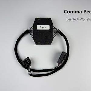 Op de afbeelding: Een zwarte Comma Pedal elektronische module met een wit label met de tekst Toyota, verbonden met een kabelboom omwikkeld met zwarte stoffen tape met twee zwarte plastic connectoren aan de uiteinden. De tekst Comma Pedal en BearTech Workshop is zichtbaar.