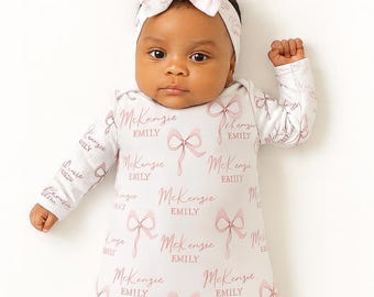 May include: A baby wearing a white sleep sack and matching headband, both adorned with pink bows and the name "McKenzie EMILY" in a repeating pattern. The baby is lying on a white surface.