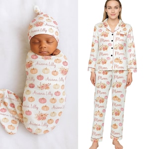 May include: A newborn baby swaddled in a white blanket and matching hat, both adorned with a pumpkin and floral pattern. The text "Ariana Lilly" is printed on the blanket and hat. A woman wears a white pajama set with a pumpkin and floral pattern and the word "Mom".