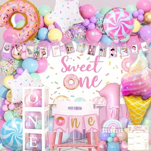 May include: A birthday party decoration set featuring a white backdrop with the text Sweet One, a donut-shaped balloon, a star balloon, a swirl candy balloon, an ice cream cone balloon, a photo banner, and a stack of clear boxes spelling ONE.