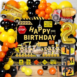 May include: A construction-themed birthday party decoration set. Includes a black backdrop with "Happy Birthday" text, balloons in yellow, orange, and black, and construction vehicle-shaped balloons. A gold number 2 balloon and clear boxes with letters and balloons are also present.