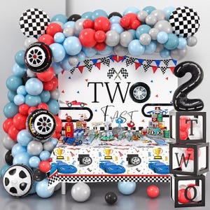 May include: A racing-themed party decoration set with a balloon arch in red, blue, and gray. Includes tire and checkered flag balloons, a banner, and a table setting with a race car tablecloth. The backdrop reads "TWO FAST".