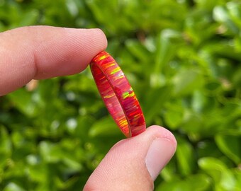 以下が含まれることがあります： 黄色とオレンジのオパールの渦巻き模様が施された、薄い赤いリングです。