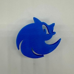 May include: A blue 3D printed Sonic the Hedgehog logo. The logo is a stylized silhouette of Sonic's head with a swirl around it.