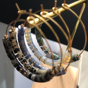 Peut inclure: Trois paires de créoles dorées avec des perles de pierres précieuses de différentes couleurs. Les perles sont dans des tons de bleu, vert et blanc.