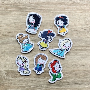 Puede incluir: Conjunto de nueve parches bordados para planchar con princesas Disney. Cada parche es blanco con una imagen de dibujos animados de una princesa. Las princesas incluyen Blancanieves, Cenicienta, Mulan, Ariel, Elsa, Anna, Rapunzel y dos versiones de Bella.