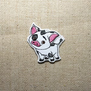 Pode incluir: Patch bordado com um porco de desenho animado com pelo branco, manchas pretas e orelhas e focinho rosa. O porco tem uma expressão amigável e é delineado em preto. O patch está em um fundo de tecido bege.