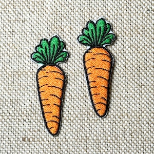 May include: Two embroidered carrot patches. Each patch features an orange carrot with green leafy tops and black outlines. The patches are on a beige fabric background.