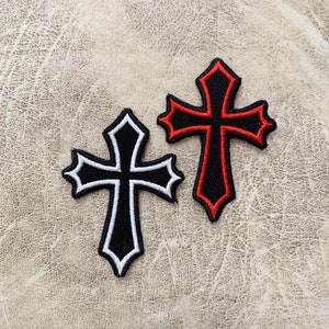 Może przedstawiać: Dwa naszywki do prasowania z ozdobnym wzorem krzyża. Jedna naszywka jest czarna z białymi szwami, a druga jest czerwona z czarnymi szwami.