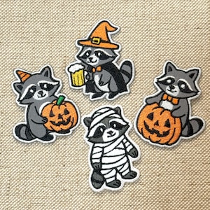 Può includere: Quattro toppe ricamate con procioni in costume di Halloween. Un procione indossa un cappello da strega e un mantello, un altro tiene in mano un boccale di birra e altri due tengono in mano zucche intagliate. Le toppe hanno un bordo bianco.