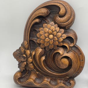 May include: A carved wooden decorative architectural element featuring floral and scroll designs. The piece is stained in a warm brown color, with detailed carvings of flowers and swirling patterns. The overall design is ornate and detailed, suitable for home decor.