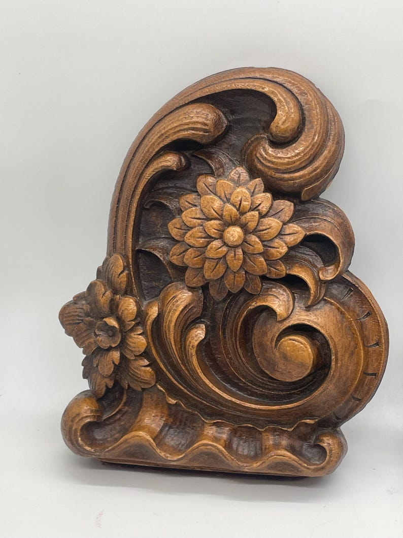 May include: A carved wooden decorative architectural element featuring floral and scroll designs. The piece is stained in a warm brown color, with detailed carvings of flowers and swirling patterns. The overall design is ornate and detailed, suitable for home decor.
