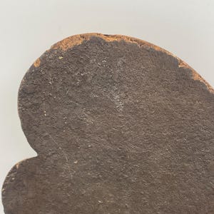 May include: Close-up of a dark brown, irregularly shaped object with a textured surface. The object has a rounded top edge with a lighter, weathered appearance. The overall shape is reminiscent of a stylized leaf or a decorative element.