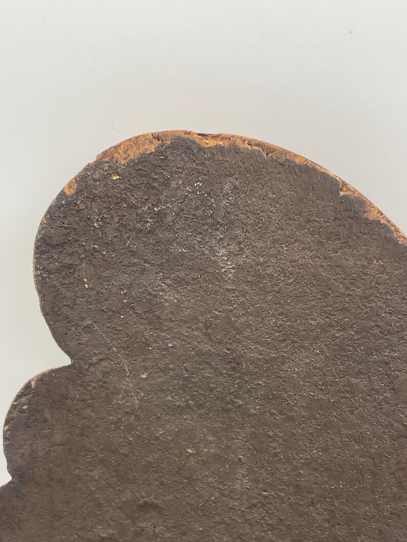 May include: Close-up of a dark brown, irregularly shaped object with a textured surface. The object has a rounded top edge with a lighter, weathered appearance. The overall shape is reminiscent of a stylized leaf or a decorative element.