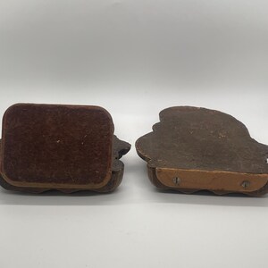 May include: Two brown wooden bookends with a decorative design. One bookend has a brown velvet backing, while the other shows the underside with a wooden base and screws. The bookends are on a white surface.