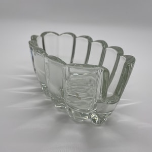 May include: Clear glass dish with a scalloped edge. The rectangular dish has a series of curved, petal-like sections. The glass is transparent, allowing light to pass through, and sits on a white surface.