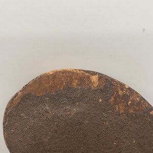 May include: Close-up of a weathered, heart-shaped wooden object. The surface is a dark brown with a textured appearance, and the edges show a lighter, aged wood color. The object appears to be antique or vintage.
