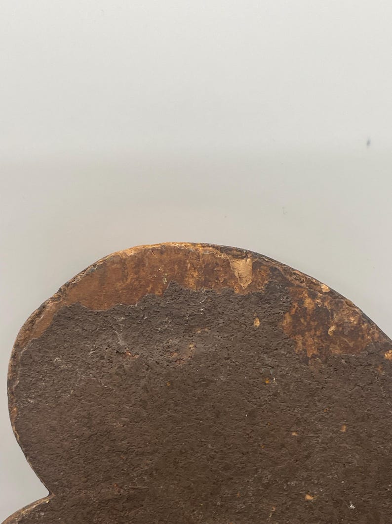 May include: Close-up of a weathered, heart-shaped wooden object. The surface is a dark brown with a textured appearance, and the edges show a lighter, aged wood color. The object appears to be antique or vintage.