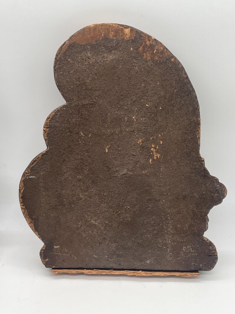 May include: A weathered, wooden decorative piece with a dark brown, textured surface. The object has an irregular, organic shape with a rounded top and a flat base. The wood shows signs of age and wear.