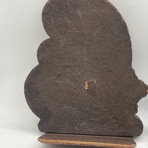 May include: A pair of brown bookends with a textured, dark brown surface. The bookends have a decorative, curved shape and sit on a rectangular base. The edges of the bookends have a lighter brown color.