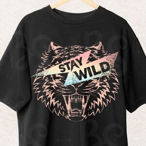 Op de afbeelding: Zwart T-shirt met een afbeelding van een tijgerkop met een roze, blauwe en gele bliksem over de ogen. De tekst "Stay Wild" staat op de bliksem.