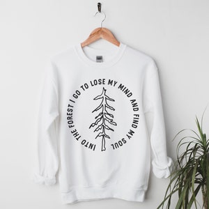 Pu&ograve; includere: Felpa bianca con una grafica nera di un albero e il testo "Into the forest I go to lose my mind and find my soul".