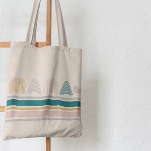 May include: A beige canvas tote bag with the word "mama" printed in a colourful, geometric font. The bag has a teal, pink and gold striped design.