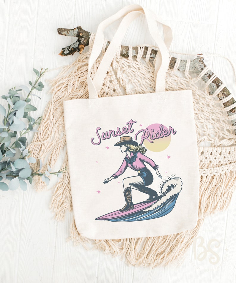 Beige tote bag displaying a Surfing Cowgirl graphic, showing a cowgirl on a surfboard with the text "Sunset Rider," ideal for beach outings and shopping