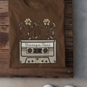 May include: A brown t-shirt with a vintage cassette tape design and the text "Vintage Soul" printed on it. The cassette tape is surrounded by stylized flowers.