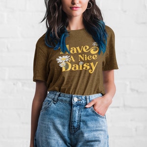 May include: A brown t-shirt with the text "Have a Nice Daisy" in yellow with white daisy flowers.