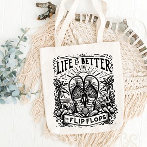 May include: A white canvas tote bag with black text and a graphic design. The text reads "Life is better in flip flops". The graphic is a pair of flip flops with palm trees and waves.