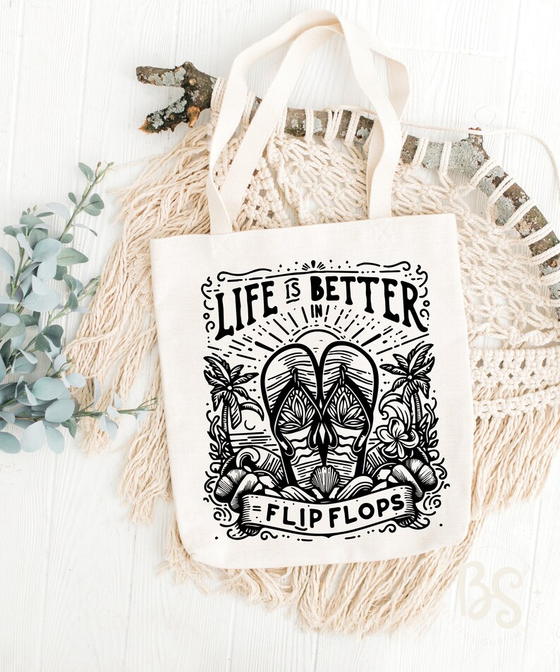 May include: A white canvas tote bag with black text and a graphic design. The text reads "Life is better in flip flops". The graphic is a pair of flip flops with palm trees and waves.