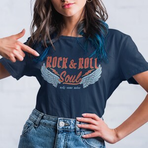 Puede incluir: Una camiseta azul marino con un gr&aacute;fico de estilo vintage que dice "Rock & Roll Soul" con alas y rayos. El texto debajo del gr&aacute;fico dice "make some noise".