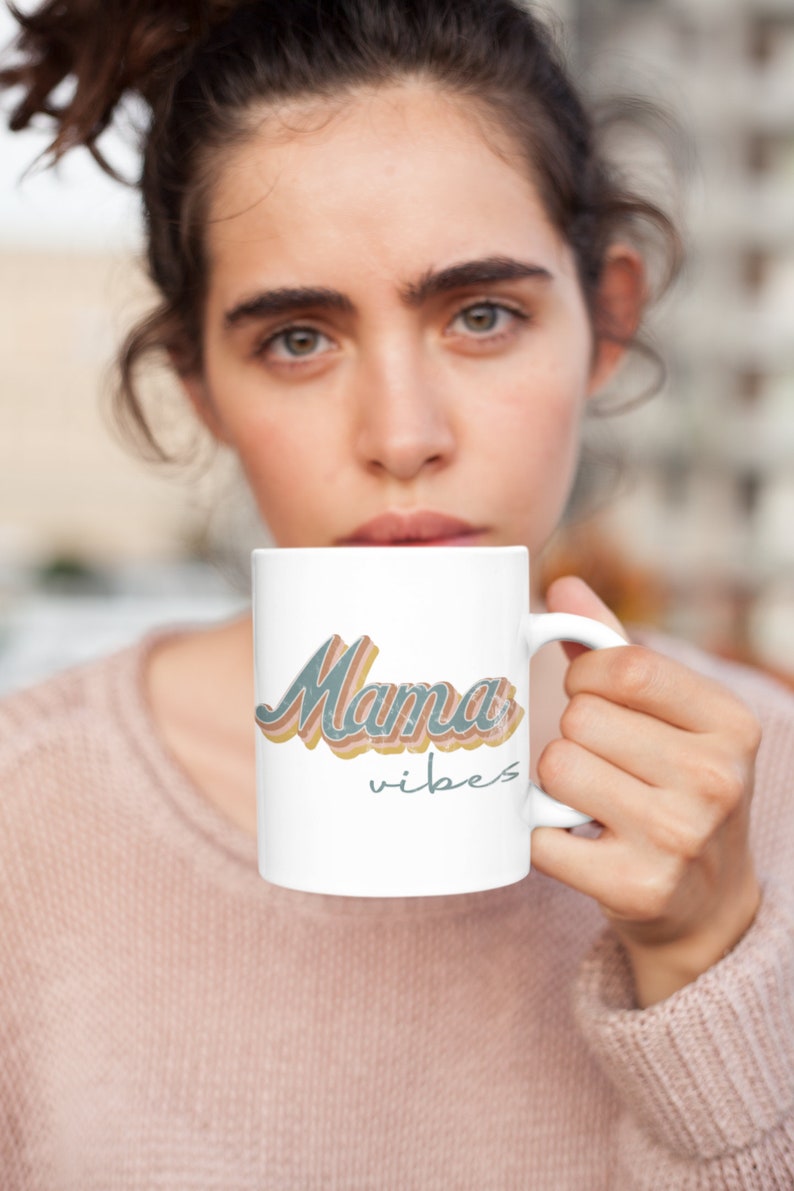 Puede incluir: Taza de cer&aacute;mica blanca con un dise&ntilde;o retro que presenta el texto "Mama vibes" en azul, naranja y rosa.