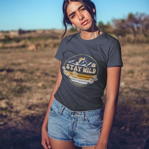 May include: A dark blue t-shirt with a graphic of mountains, a sun, and daisies. The graphic has the text "Stay Wild" in a yellow circle.