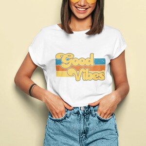 May include: A white t-shirt with a retro-style graphic that says "Good Vibes" in yellow and orange letters with blue and orange stripes behind the text.