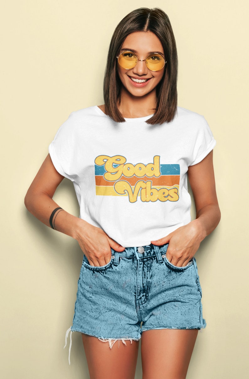 May include: A white t-shirt with a retro-style graphic that says "Good Vibes" in yellow and orange letters with blue and orange stripes behind the text.