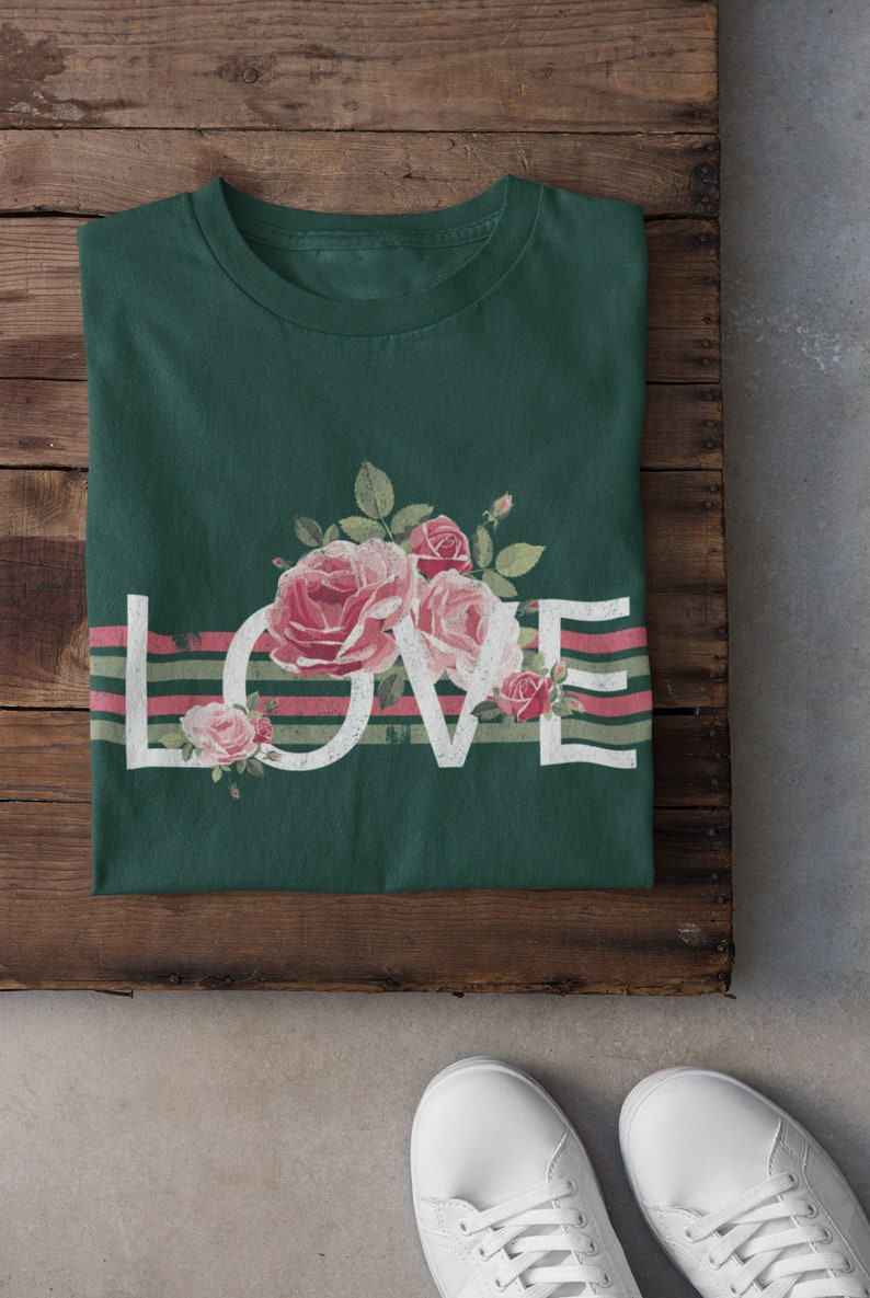 May include: A green t-shirt with a white "LOVE" graphic and pink roses. The graphic is layered over pink and green stripes.