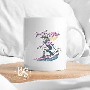 White ceramic mug with a Surfing Cowgirl design, featuring a stylish cowgirl riding a surfboard with the text "Sunset Rider," perfect for sublimation projects.