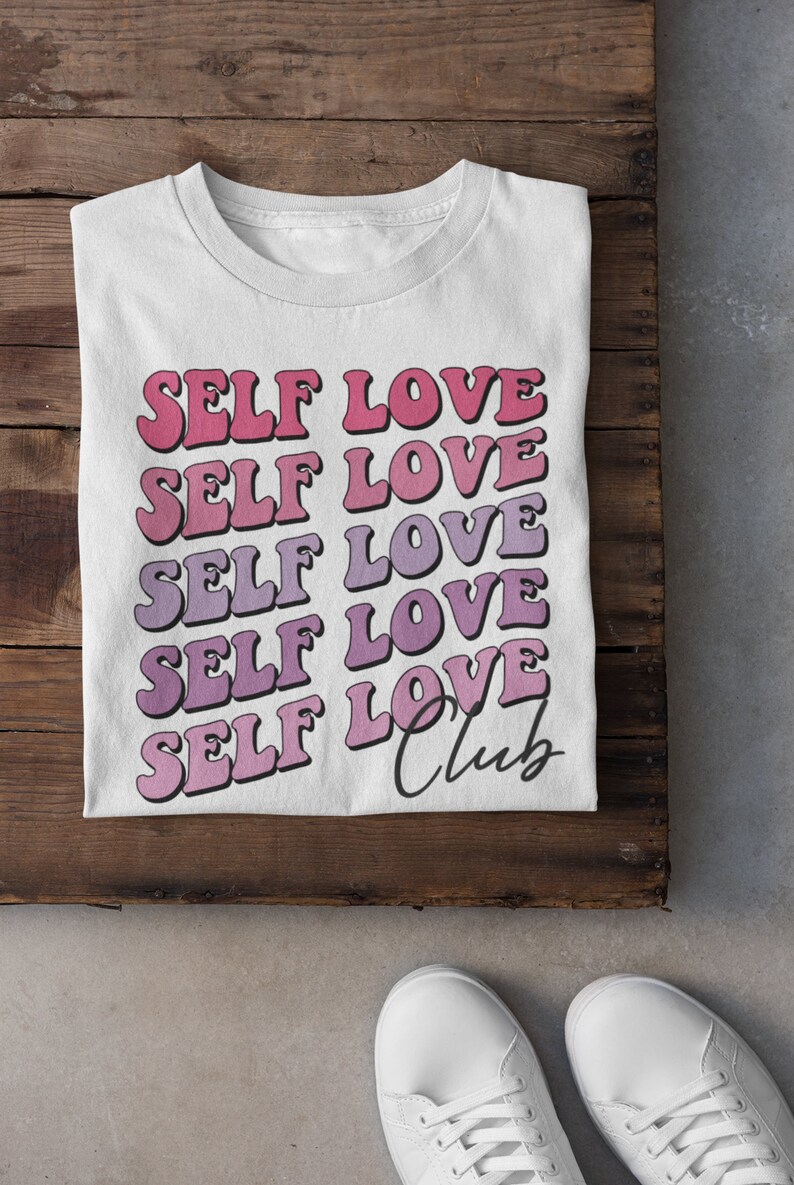 May include: White t-shirt with the text "SELF LOVE" repeated five times in a gradient of pink and purple. The text "Club" is written in cursive below the repeated text.