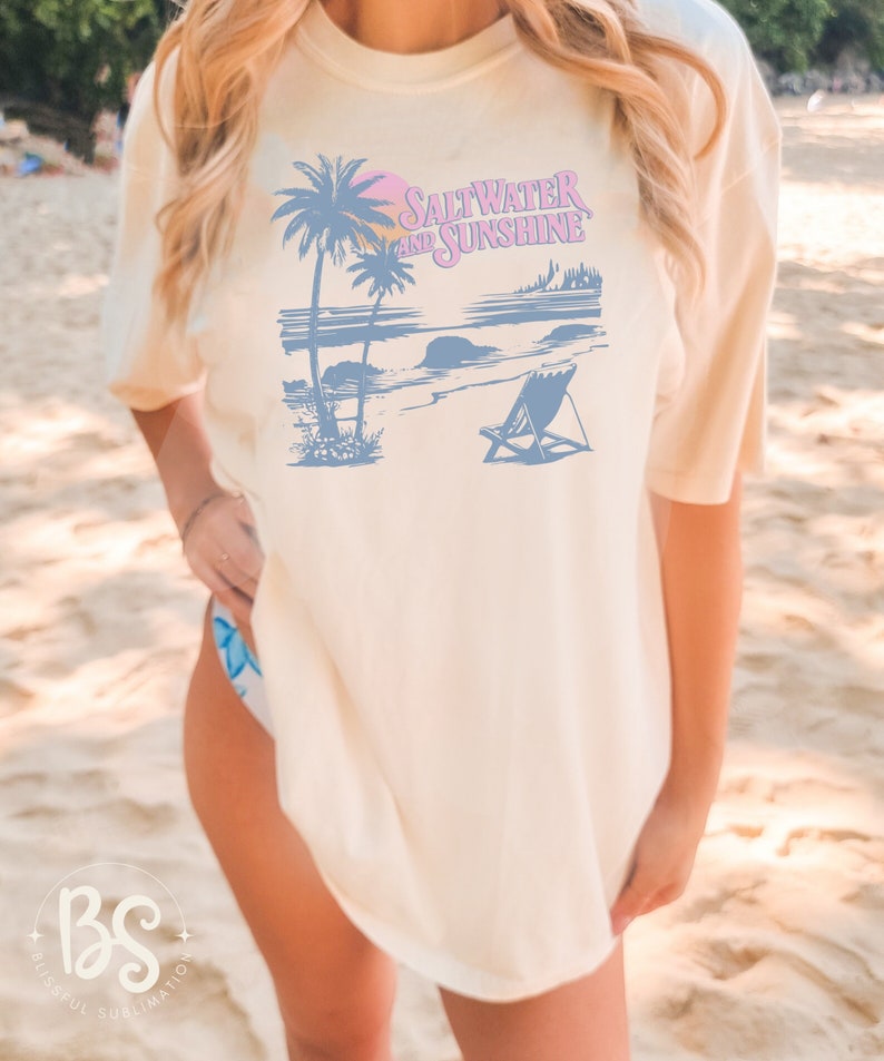 May include: A white t-shirt with a blue and pink graphic design of palm trees, a beach scene, and the text "Saltwater and Sunshine".