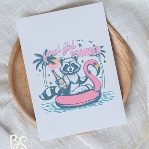 May include: A raccoon wearing a blue shirt sits on a pink flamingo pool float with a bottle of beer in its hand. The raccoon is surrounded by palm trees and stars. The text "feral girl summer" is written above the raccoon.