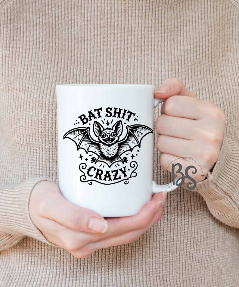K&ouml;nnte beinhalten: Wei&szlig;e Keramiktasse mit einer schwarz-wei&szlig;en Illustration einer Fledermaus mit dem aufgedruckten Text "Bat Shit Crazy".