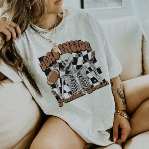 Puede incluir: Una camiseta blanca con un gr&aacute;fico de un esqueleto sosteniendo un bal&oacute;n de f&uacute;tbol y el texto "Dead Inside But It's Football Season".