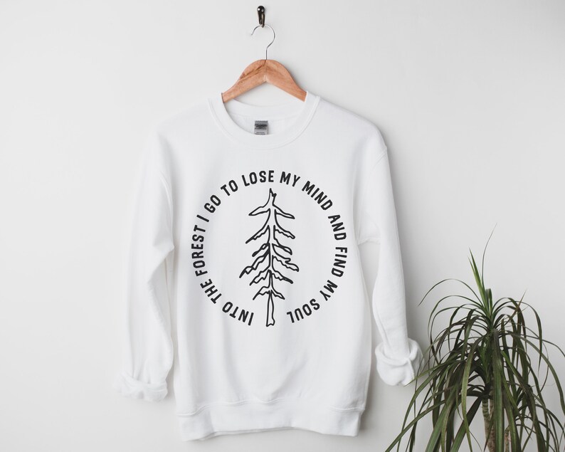 Pu&ograve; includere: Felpa bianca con una grafica nera di un albero e il testo "Into the forest I go to lose my mind and find my soul".