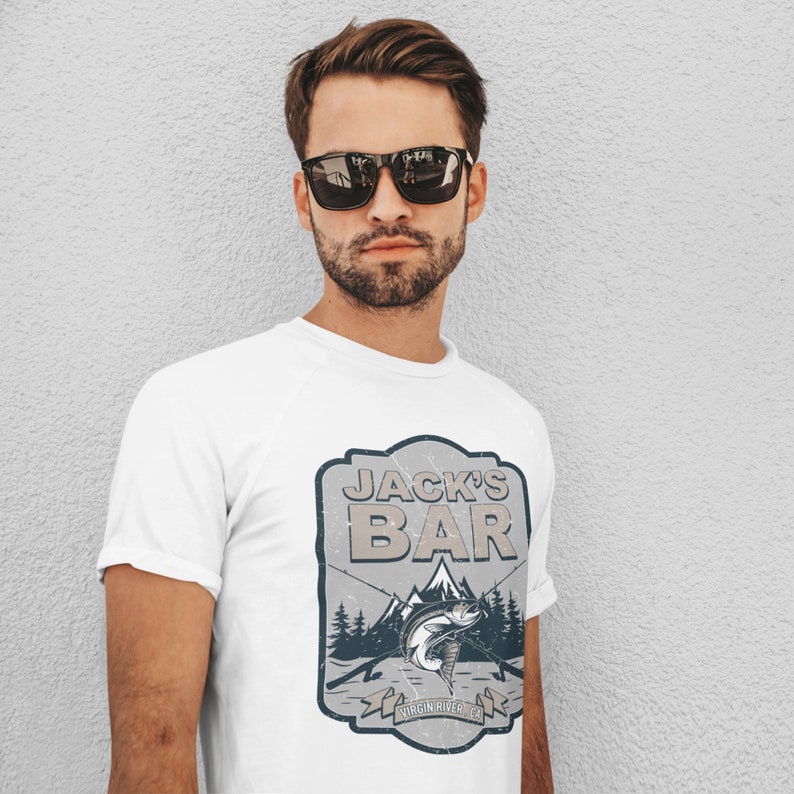 May include: White t-shirt with a vintage-style logo that says "Jack's Bar" with a mountain scene and a fish. The logo also says "Virgin River, CA".